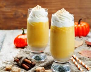 two tall glasses of low carb pumpkin spice smoothie topped with whipped cream and sprinkled with pumpkins spice.