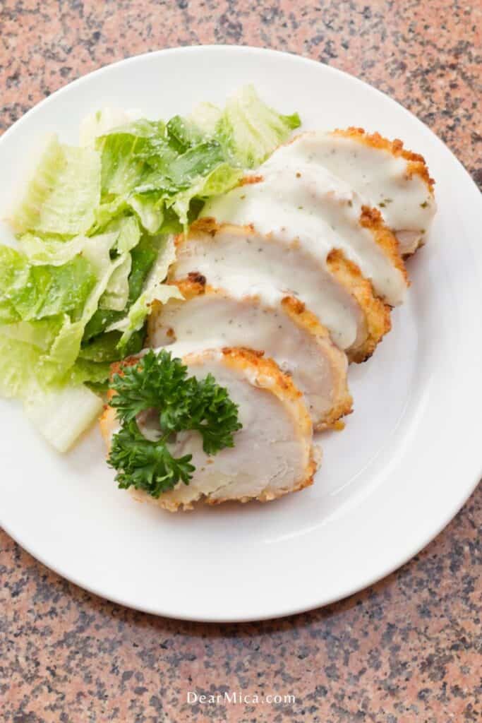 sliced keto chicken cordon blue with creamy sauce and a side salad served on a white plate.