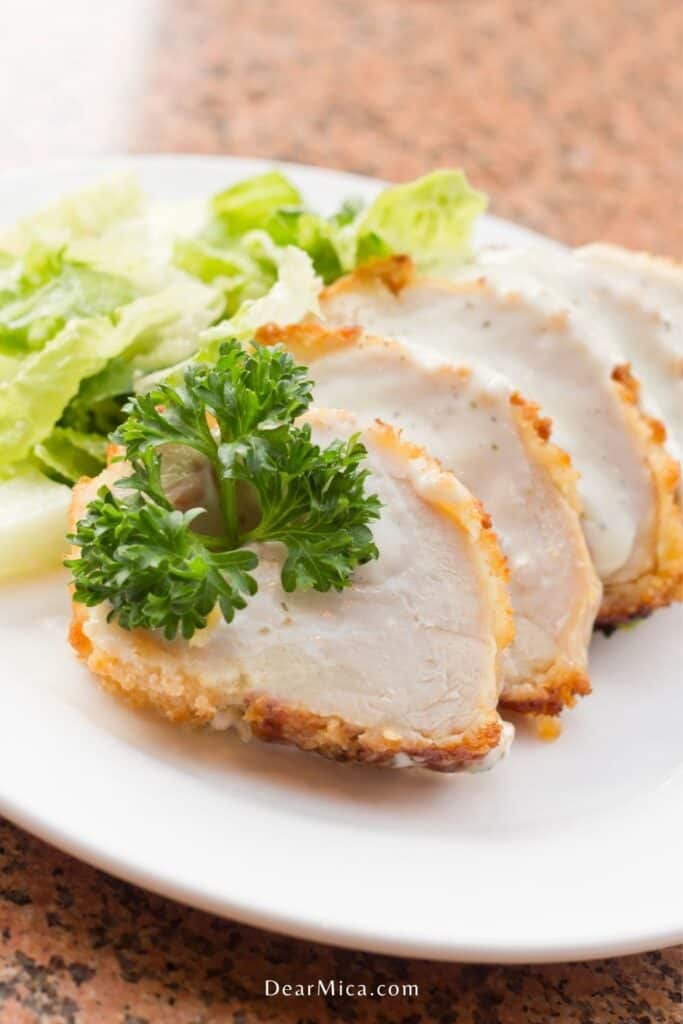 side view of sliced keto chicken cordon blue with creamy sauce and a side salad served on a white plate.