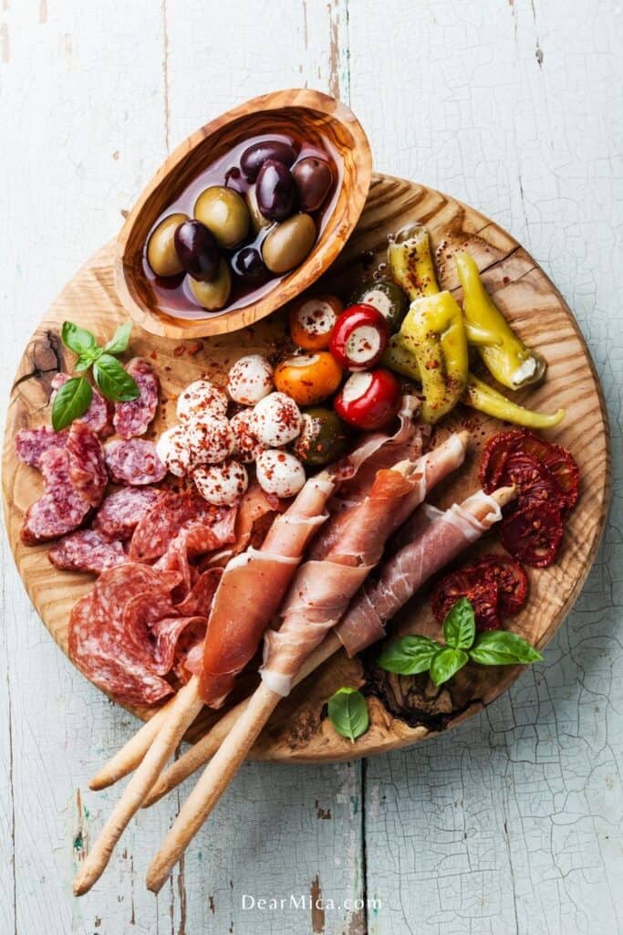 top view of a Low Carb Antipasto with olives, prosciutto, mini mozzarella balls, salami, chorizo and mini green peppers and sun dried tomatoes served on a wooden board.