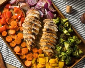 Keto sheet pan chicken with rainbow veggies such as carrots, red, yellow and green peppers, broccoli and purple onions.