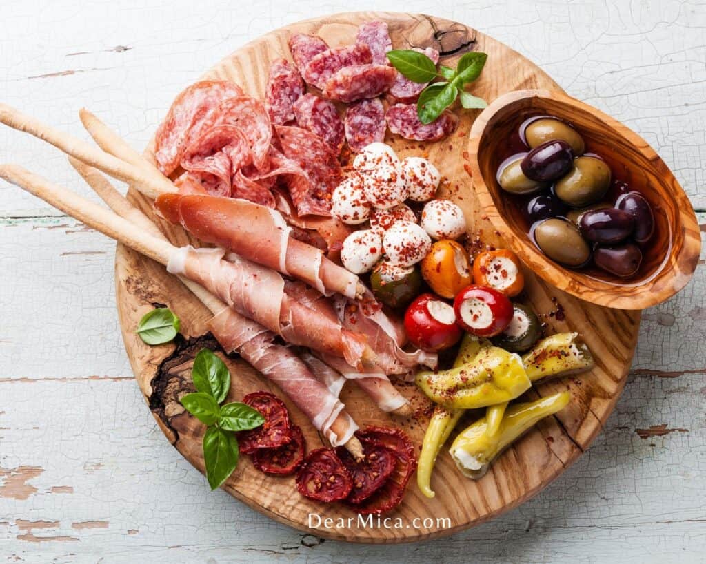 top view of a Low Carb Antipasto with olives, prosciutto, mini mozzarella balls, salami, chorizo and mini green peppers served and sun dried tomatoes on a wooden board.