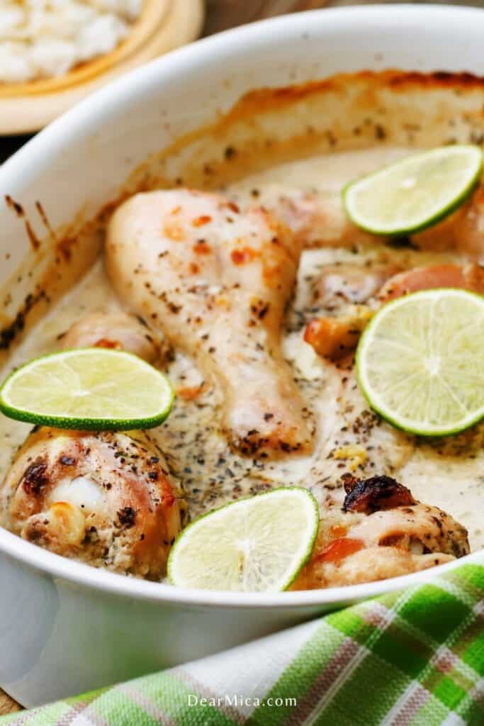 Side view of low carb coconut lime chicken legs on a white baking dish and garnished with lime slices.