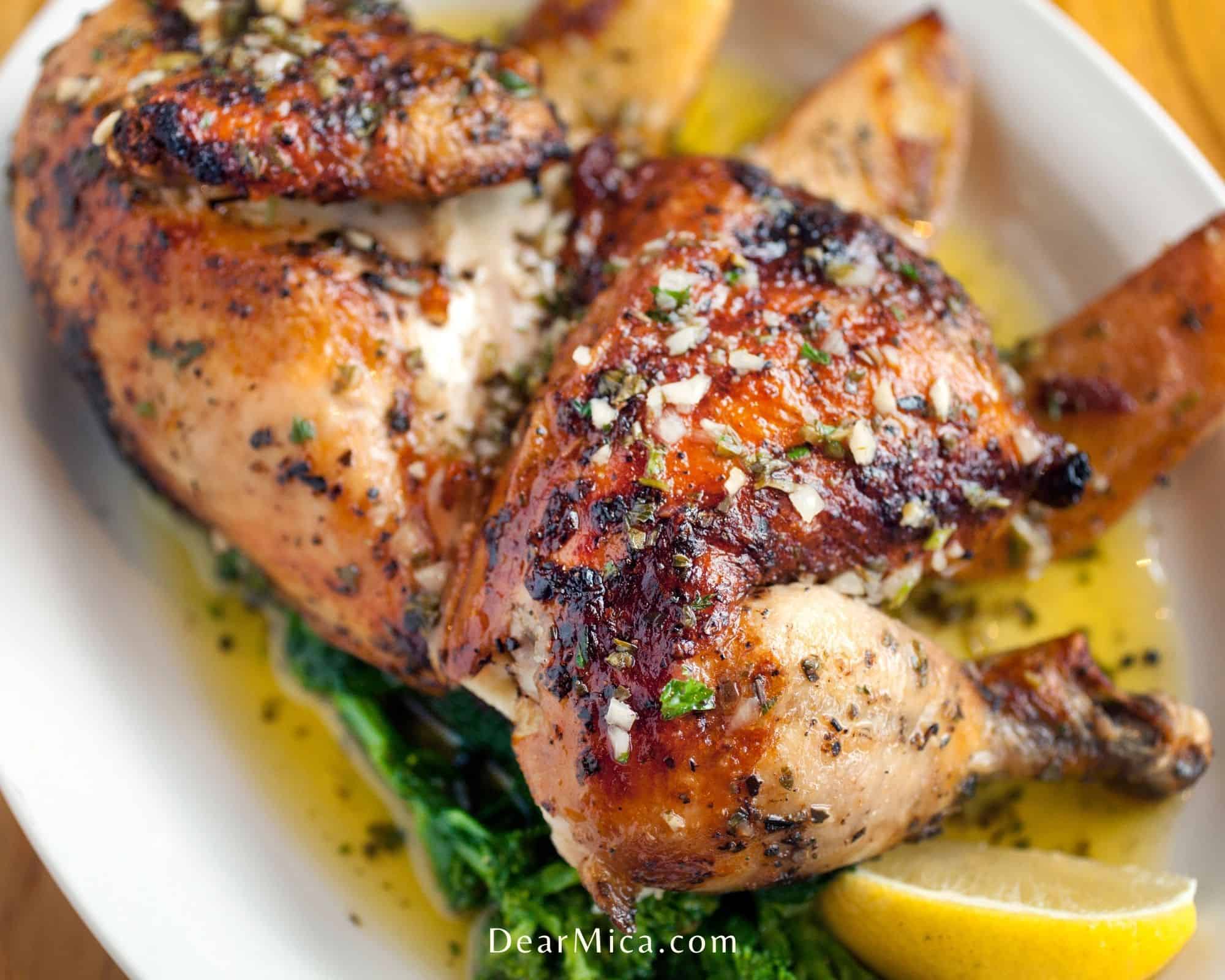 Side view of Half roasted chicken served on a white oval plate garnished with lemon wedges.