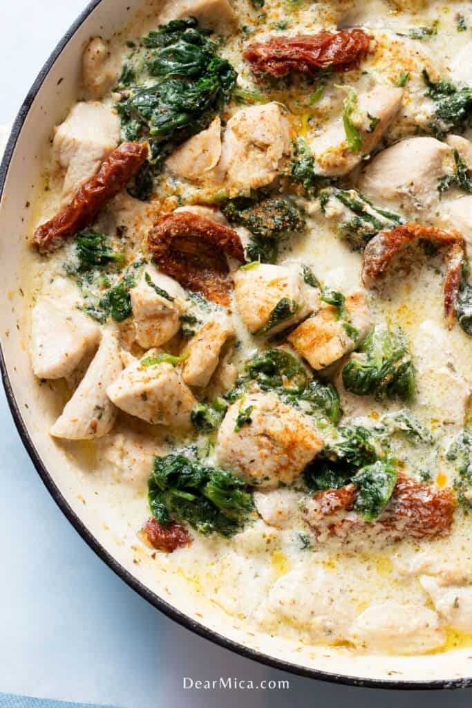 Top view of a creamy keto tuscan chicken with sun dried tomatoes and spinach on a white cast iron pan.