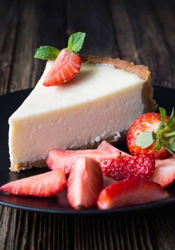 No Bake Keto Cheesecake slice with fresh strawberries on a black plate with wooden table as background.