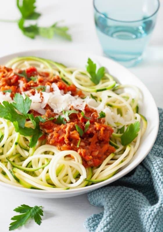 Side view of a Slow cooker noodles with meat sauce and shaved parmesan on a white plate on a white background.