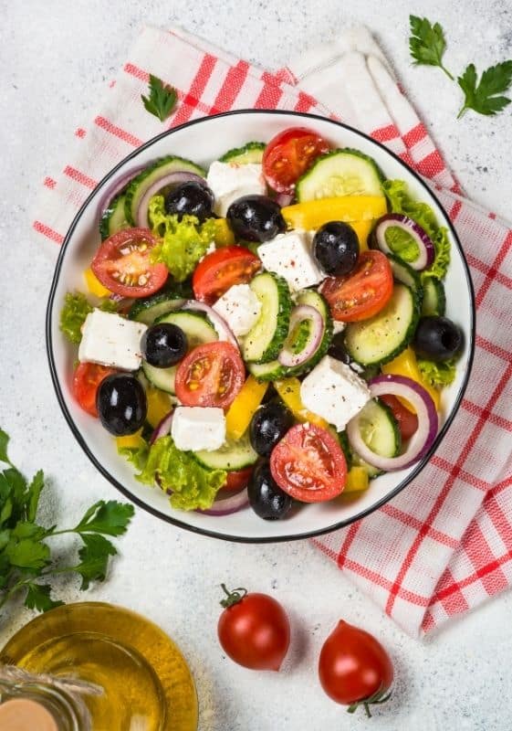 Top view of a Keto Mediterranean Greek Salad bowl on a white background with a red strip white fabric napkin.