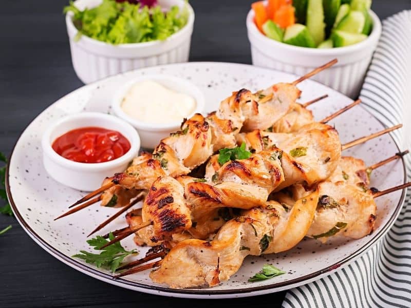 Top view of grilled chicken satay (low carb) on a plate served with tzatziki sauce on the side.