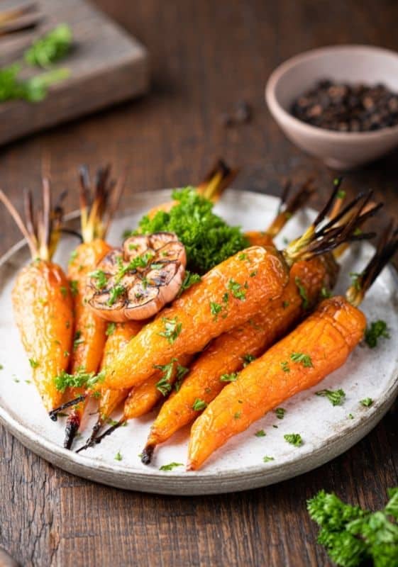 Side view of keto grilled carrots served on a white plate on a wooden table.