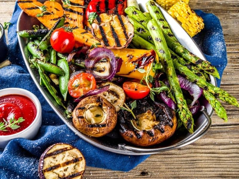 Top view of keto mixed grilled vegetables on a platter on a wooden background.