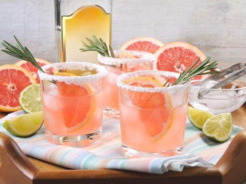 Side view of 3 Low carb sparkling Paloma cocktails garnished with orange wedges and rosemary spring.