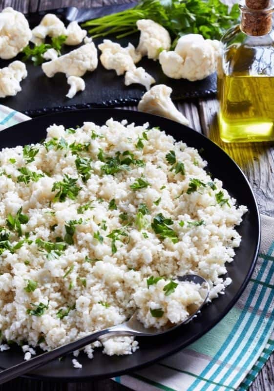 view of a Cilantro Lime Cauliflower Rice served on a black plate on a wooden table.