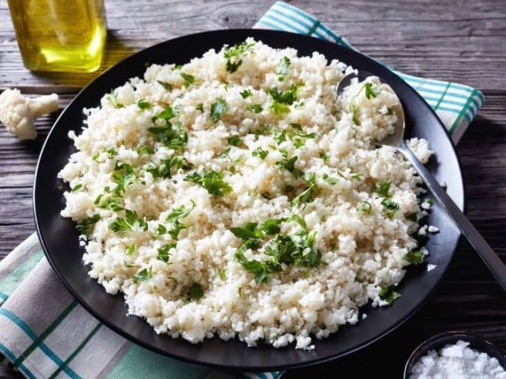 view of a Cilantro Lime Cauliflower Rice served on a black plate on a wooden table.