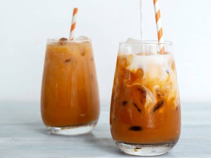 Side view of two glasses of keto Thai iced tea with straws on a gray background.