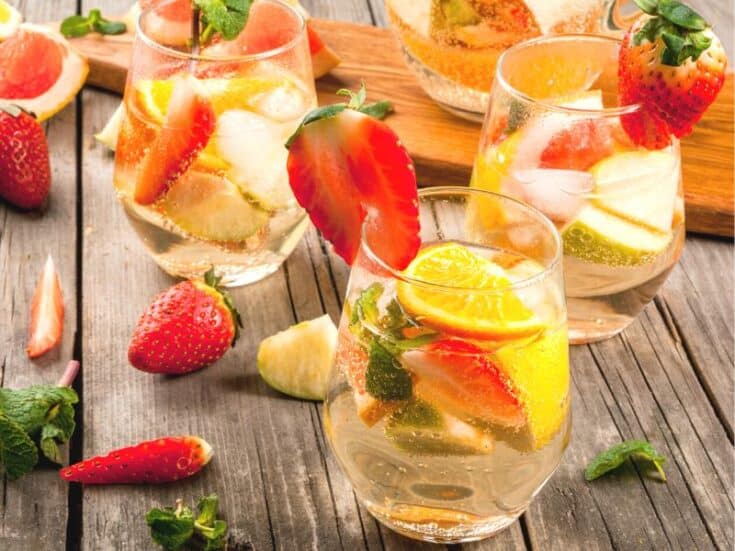 Three keto white sangria glasses on a wooden table garnisheed with strawberries and lemon wedges.